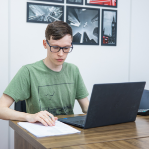 homem branco, cabelo castanho claro, usando óculos e camiseta verde, sentado na frente do computador.
